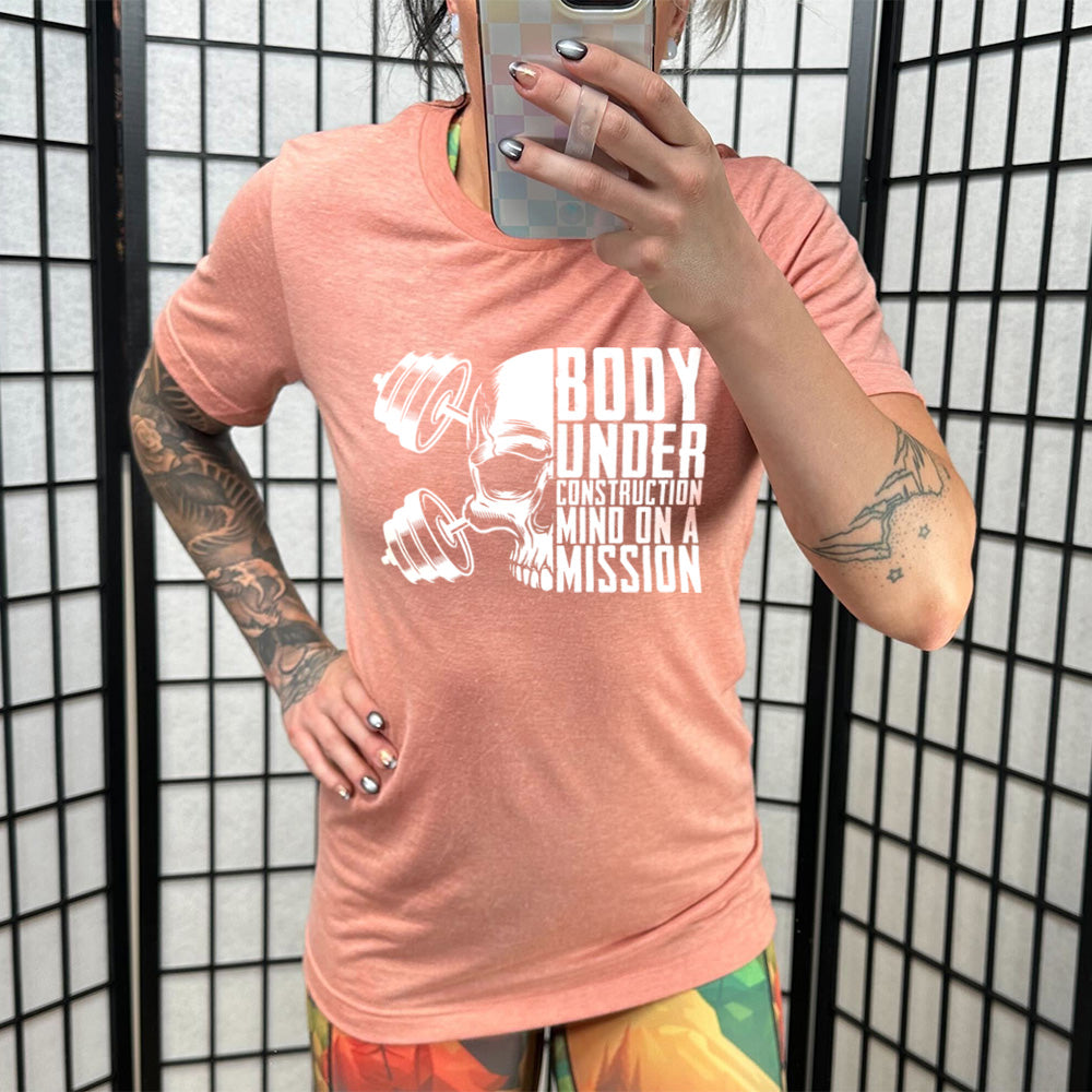 coral shirt with the text "Body Under Construction, Mind on a Mission" on it