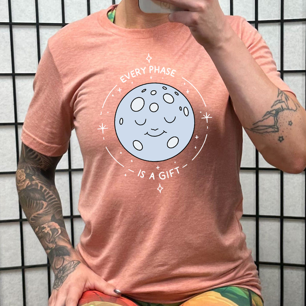 peach shirt with the text "Every Phase Is a Gift" on it