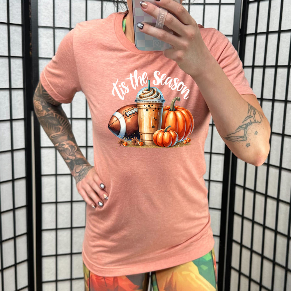 peach shirt with a football, coffee and pumpkin graphic on it with the quote "tis the season" on it