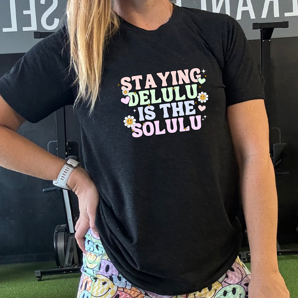 black shirt with the text "Staying Delulu Is The Solulu" on it