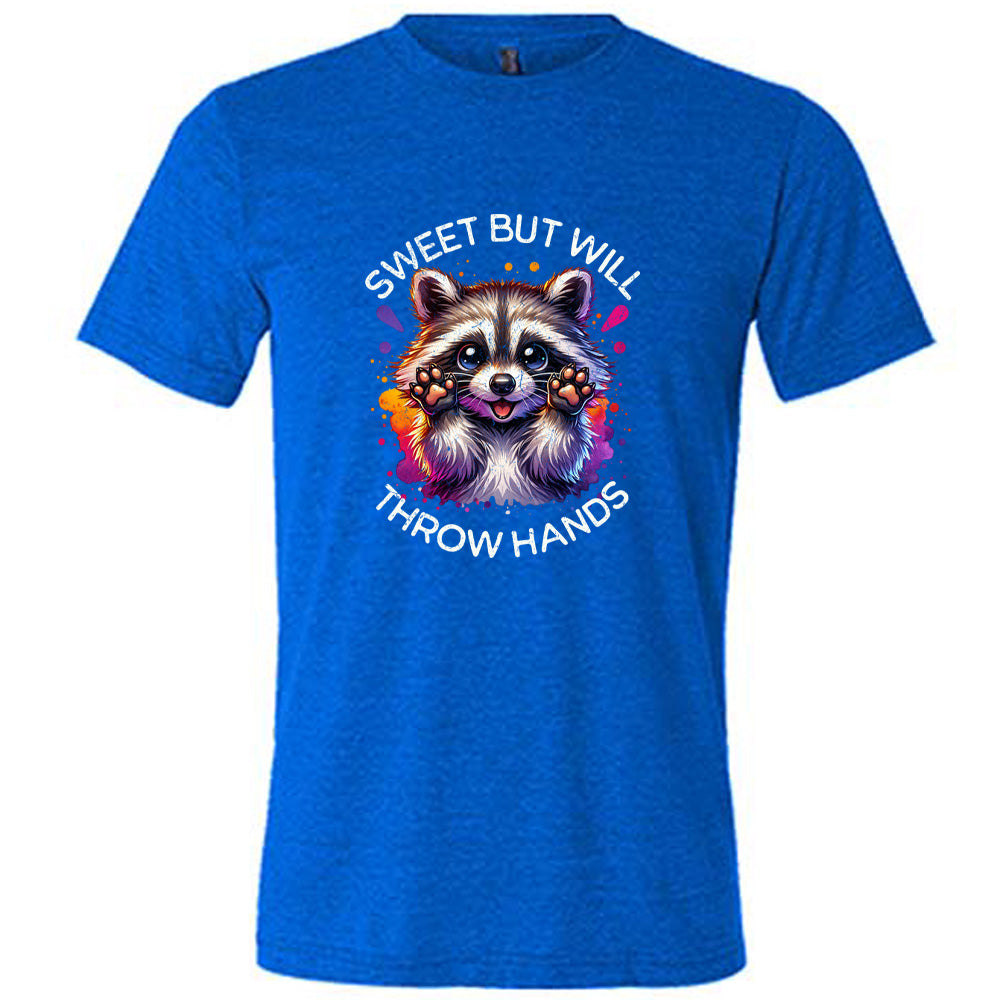 blue shirt with the text "Sweet But Will Throw Hands" and a graphic of a raccoon on it