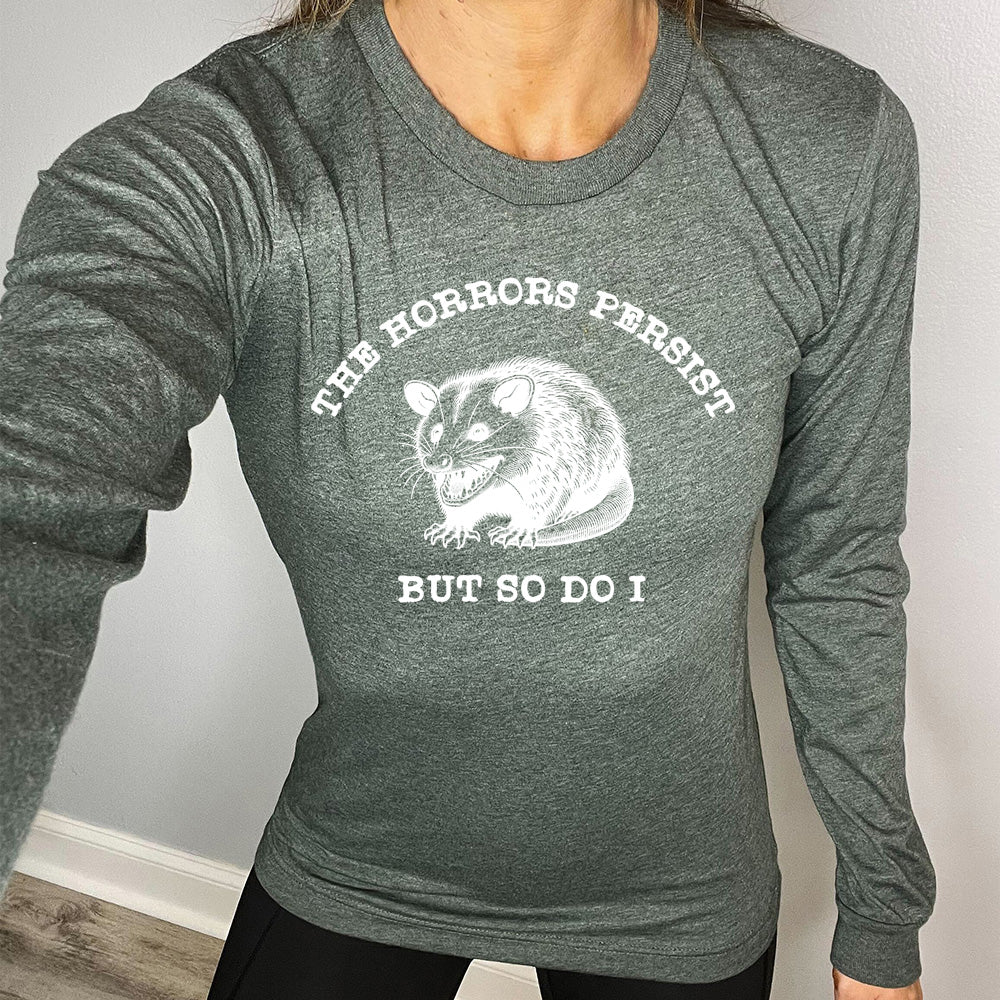 green shirt with the text "The Horrors Persist But So Do I" on it