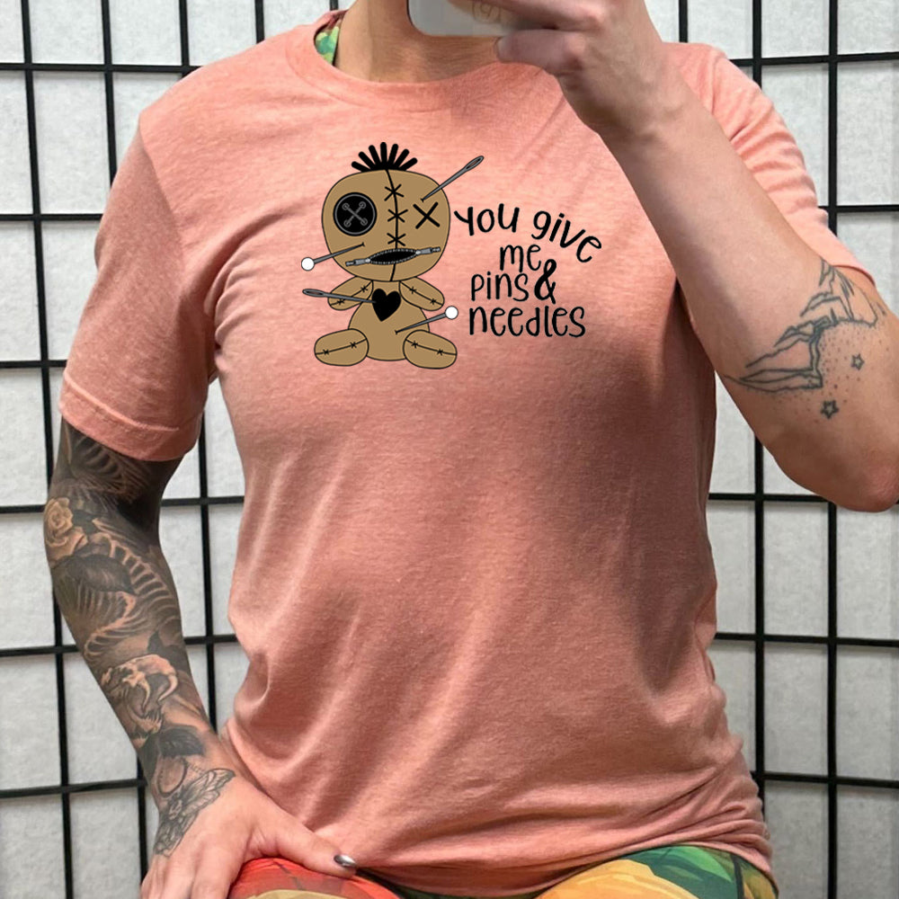 peach shirt with a voodoo doll graphic and the quote "You Give Me Pins And Needles" on it