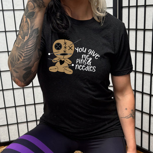 black shirt with a voodoo doll graphic and the quote "You Give Me Pins And Needles" on it