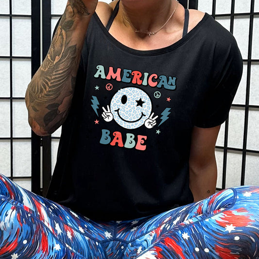 black slouchy tee with the saying "american babe" and a smiley face with peace signs and lightning bolts