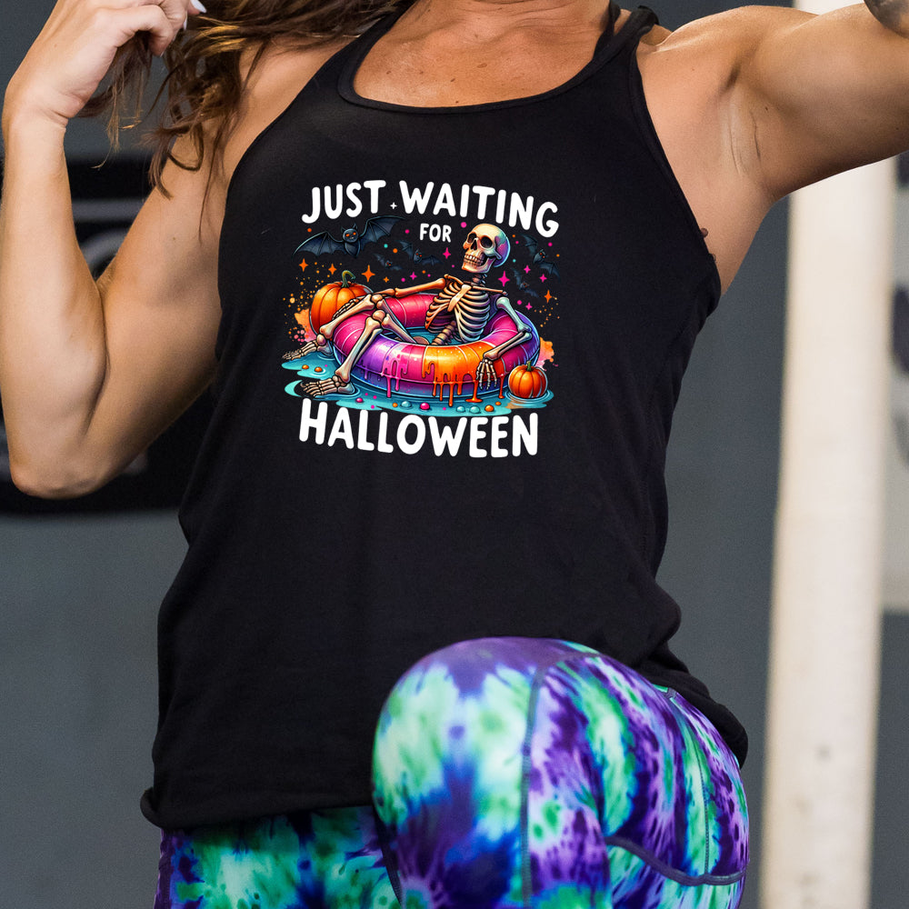 model wearing the black shirt with a colorful skeleton graphic in the center with the quote "Just Waiting For Halloween" on it