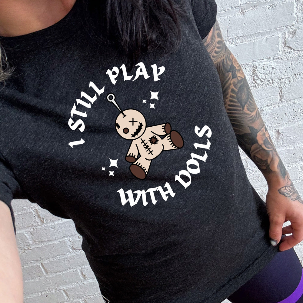 black shirt that has a voodoo doll graphic and the text "i still play with dolls" on it