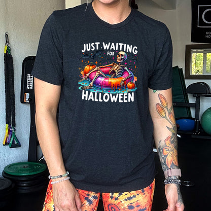 model wearing the black shirt with a colorful skeleton graphic in the center with the quote "Just Waiting For Halloween" on it