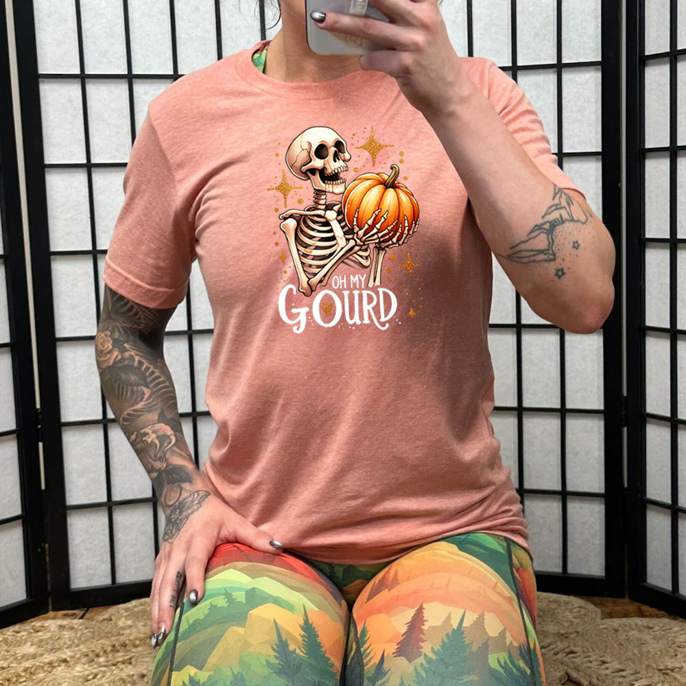 peach colored shirt with a skeleton holding a pumpkin graphic on it